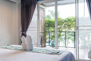 Une chambre d’hôtel avec un lit, une fenêtre avec des rideaux, un balcon et une vue sur la verdure.