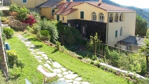A residential property with a stone pathway leading to a house with a tiled roof and a garden with various plants and a small pond.