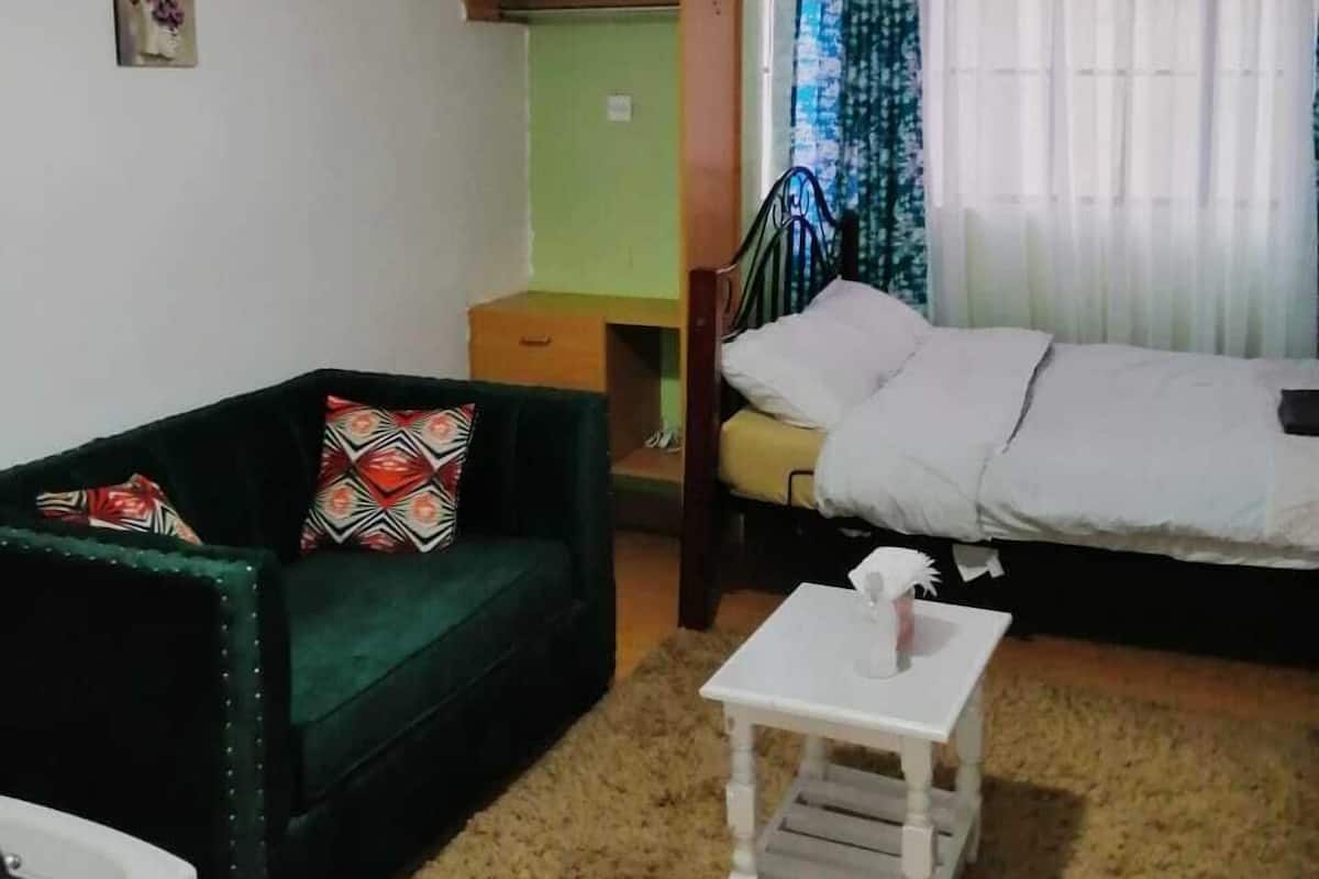 A room with a green sofa, a bed, a small white table, and a hanging light fixture.