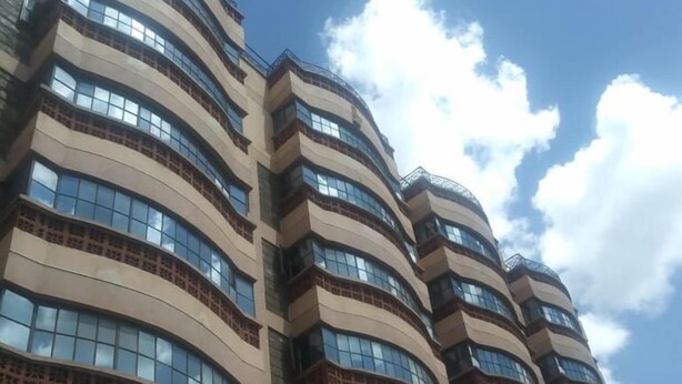 Un immeuble à plusieurs étages doté d’une façade incurvée, de grandes fenêtres et d’une clôture métallique à sa base.