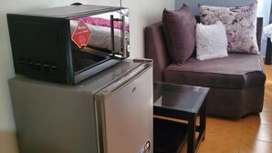 Un espace de vie compact comprenant un réfrigérateur, une petite table, un canapé et un téléviseur à écran plat fixé au mur.