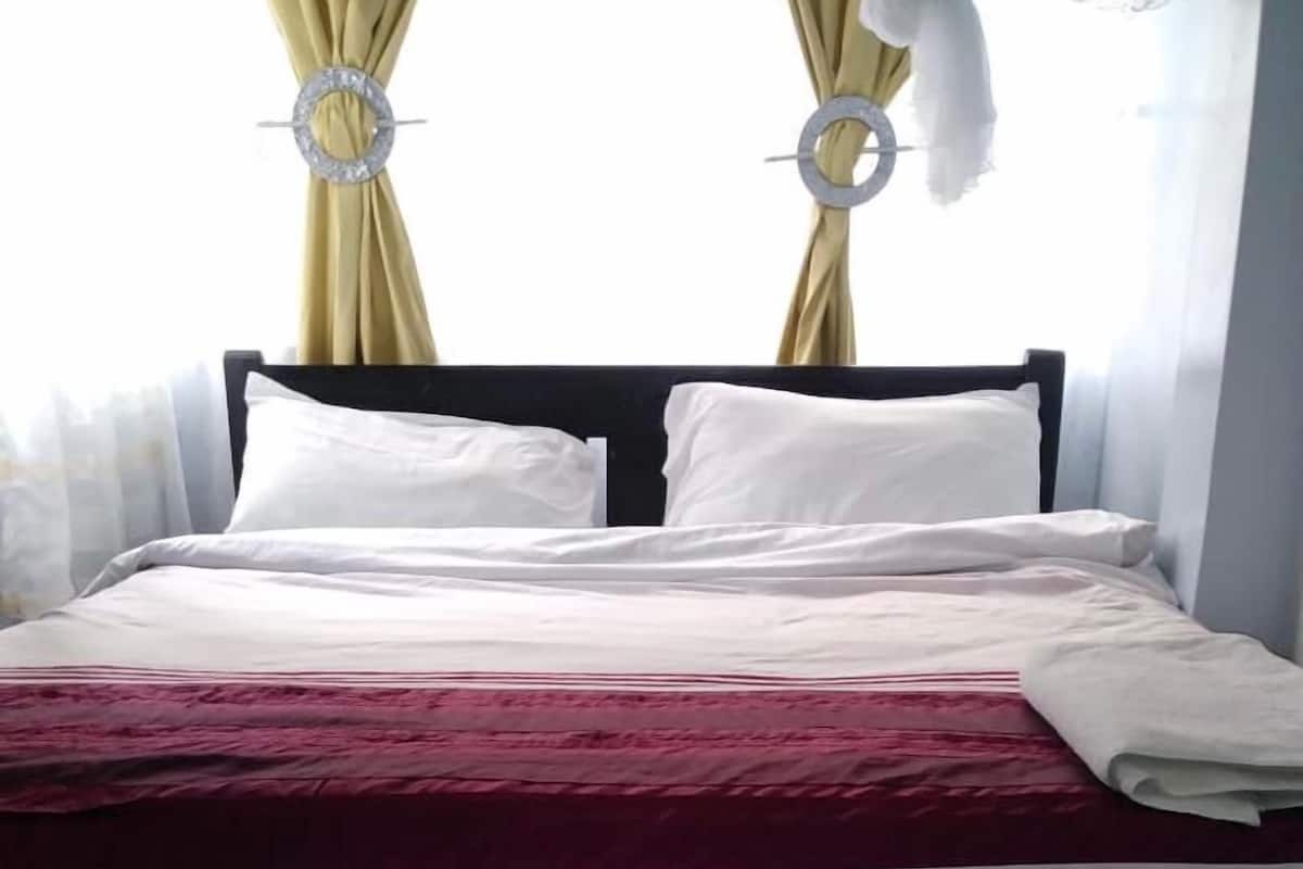 A neatly made bed with white and maroon bedding, a dark headboard, and two circular wall decorations.