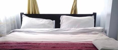 A neatly made bed with white and maroon bedding, a dark headboard, and two circular wall decorations.