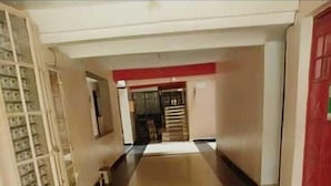 Un couloir avec un sol carrelé, un mur rouge et un escalier sur la gauche.