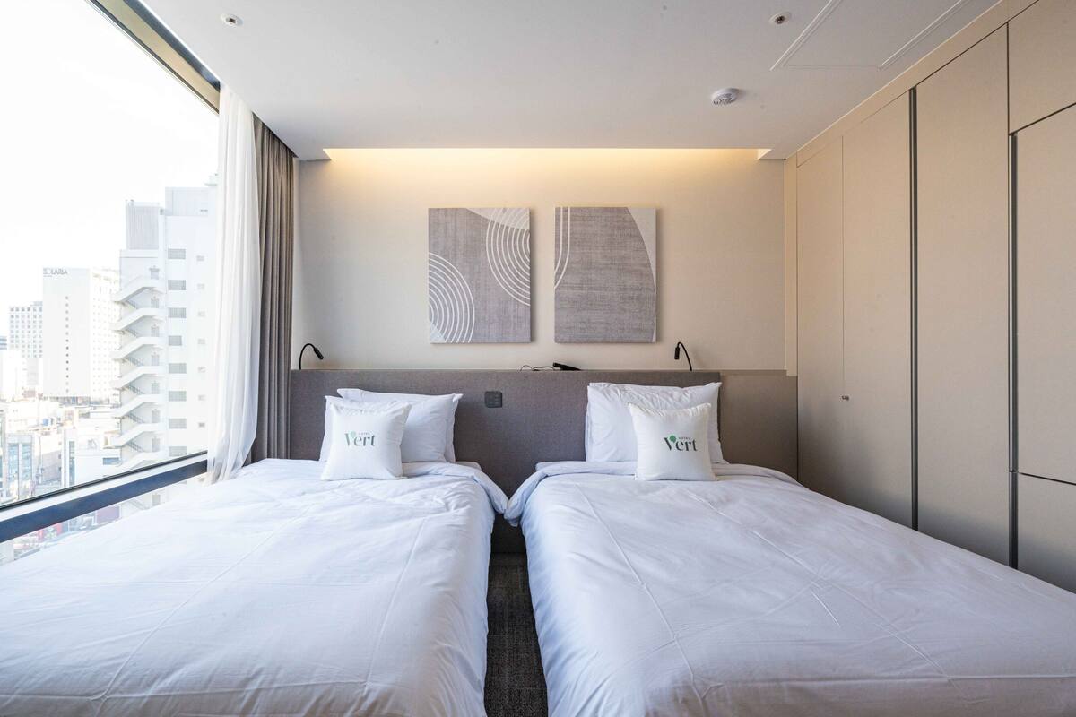 A hotel room with two beds, a city view, and artwork on the wall.
