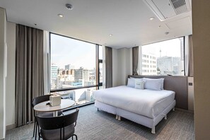 Une chambre d’hôtel avec une grande fenêtre, un lit, un bureau et une chaise.