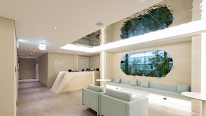 A modern reception area with a seating area, a reception desk, and a large window with a view of greenery. - Hotel Vert (Seoul)