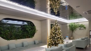 A modern interior with a seating area, a Christmas tree, and a large window with a view of greenery. - Hotel Vert (Seoul)