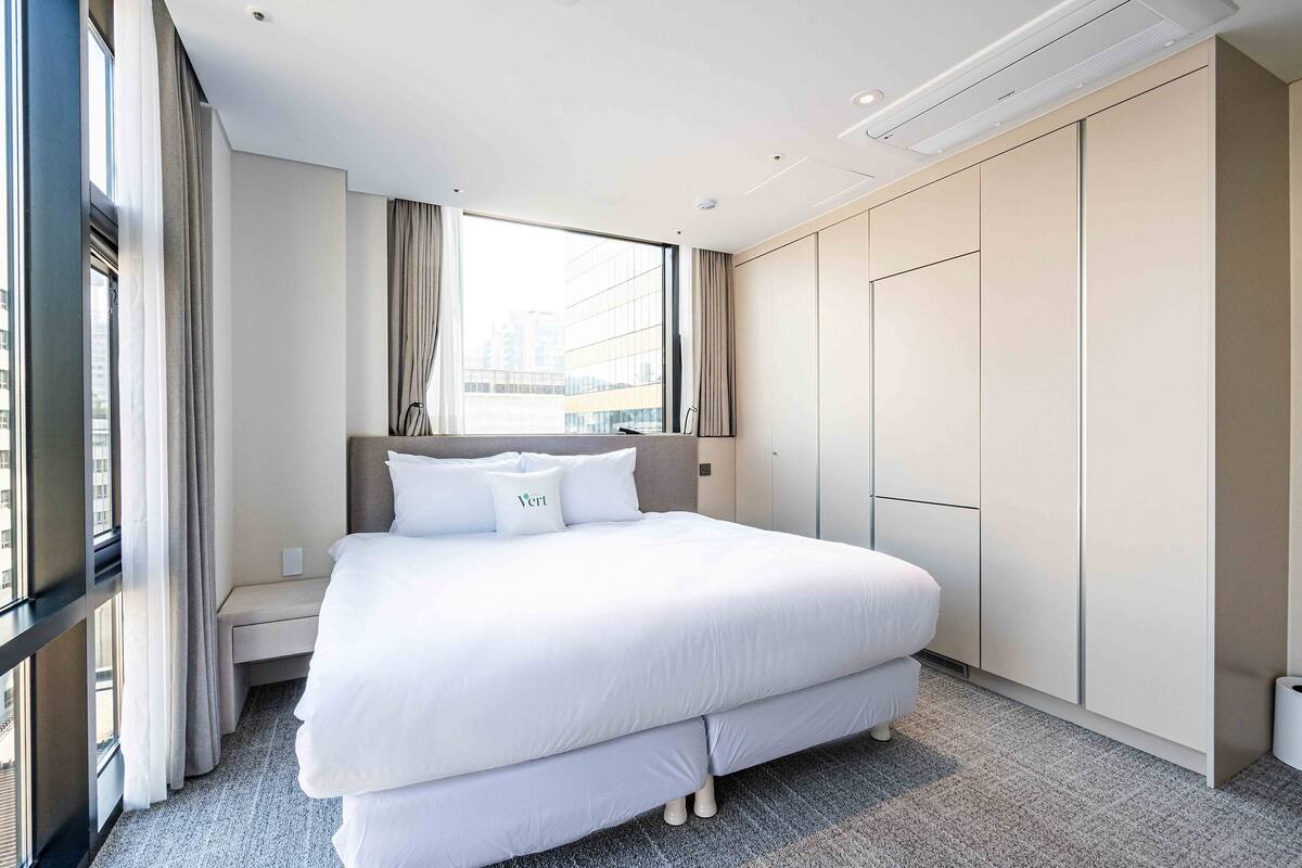 A modern hotel room with a large bed, a wardrobe, and a view of the city through the window.