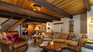 Una sala de estar acogedora con muebles de cuero, techo de madera y una escalera que lleva a otra habitación.