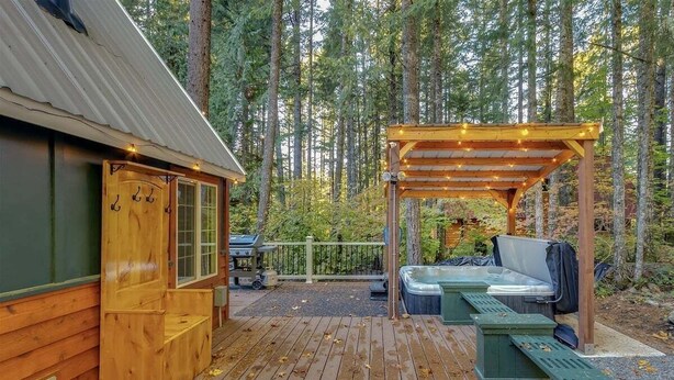 Una cabaña de madera con terraza, jacuzzi y pérgola con luces colgantes.