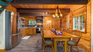 Interior de una cabaña de madera con comedor, cocina y un ventanal grande.