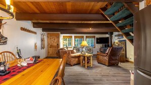 Una sala de estar acogedora con techo de madera, una mesa de comedor con mantel a cuadros rojo y negro, y una escalera que conduce a un nivel superior.