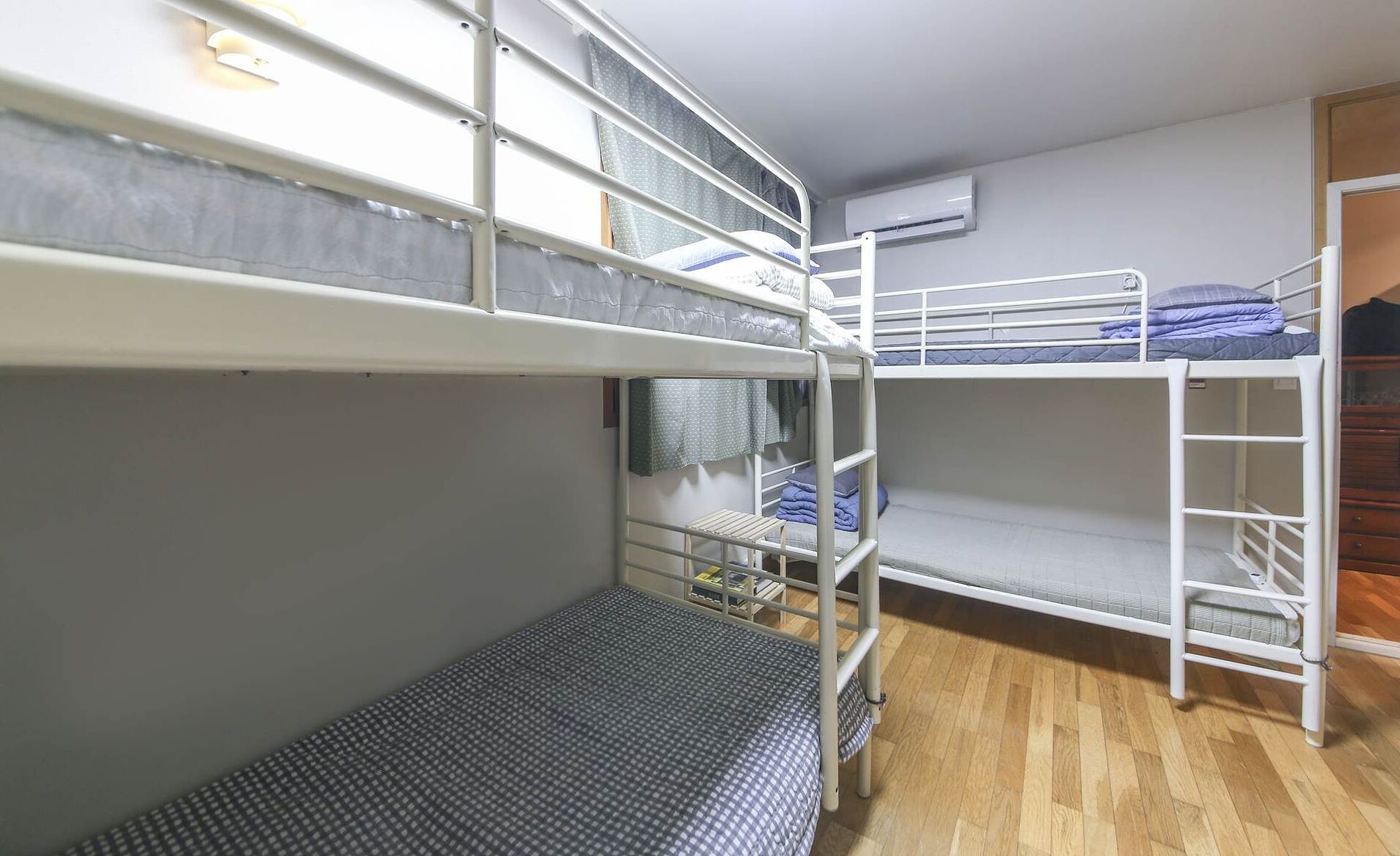 A bunk bed room with a wooden floor, a window with curtains, and an air conditioning unit on the wall.