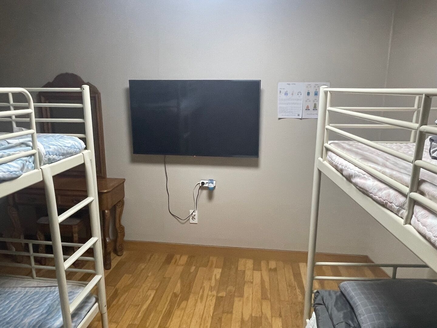 Una habitación con dos literas, piso de madera, televisor de pantalla plana montado en la pared y una pequeña mesa de madera.