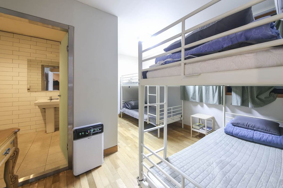 Un dormitorio con literas, una mesita pequeña, una estantería con libros y una ventana.