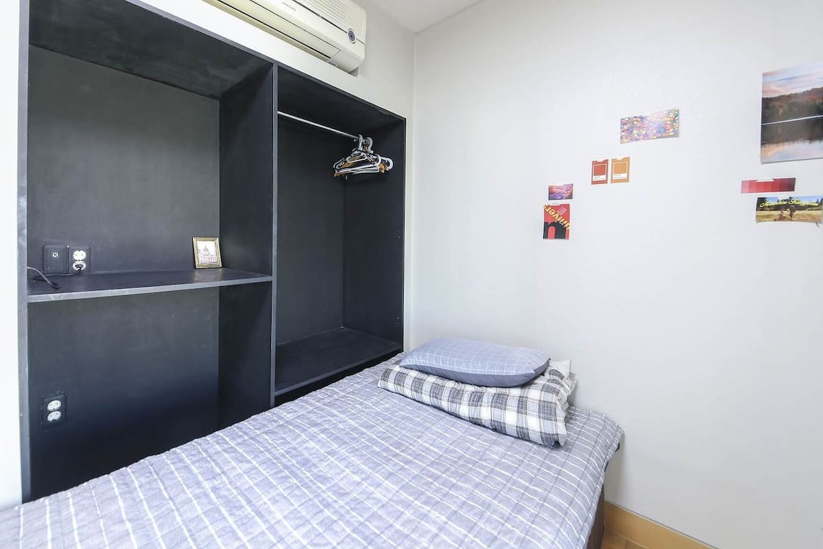 Un dormitorio pequeño y moderno con cama, un armario con estantes y aire acondicionado de pared.