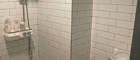 A small, tiled bathroom with a shower, toilet, and a shelf with toiletries.