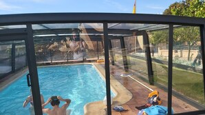 Una piscina con paredes de vidrio, un borde arenoso, un utensilio para limpieza de piscinas y un traje de baño azul sobre el borde.