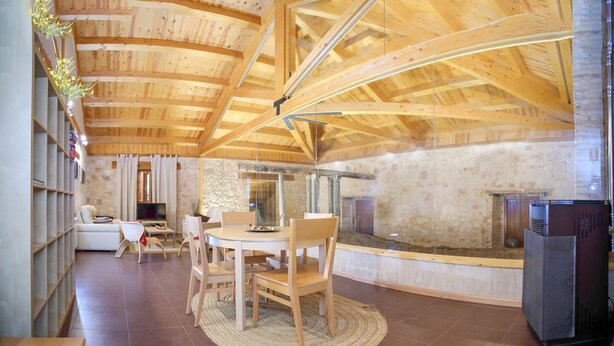 Un interior moderno con techo de madera, paredes de piedra, una mesa redonda de comedor y una chimenea.