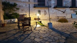 Un patio al aire libre con suelo de piedra, una mesa y sillas de madera, y una sombrilla colgante.