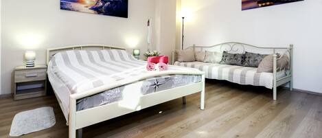 A bedroom with a bed, a sofa, wooden flooring, and wall art.