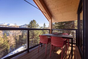 A wooden deck with a table and chairs, overlooking a snowy mountain and forest. - Natural chalet with sauna and hot tub (Turrach)