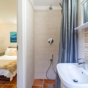 A bathroom with a shower, a sink, and a bed visible in the adjacent room. - Lilliput Apartment - P IVA (Bellagio)