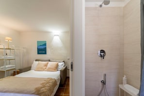 A hotel room with a bed, a bedside table, a wall-mounted lamp, a shower with a handheld showerhead, and a towel rack. - Lilliput Apartment - P IVA (Bellagio)