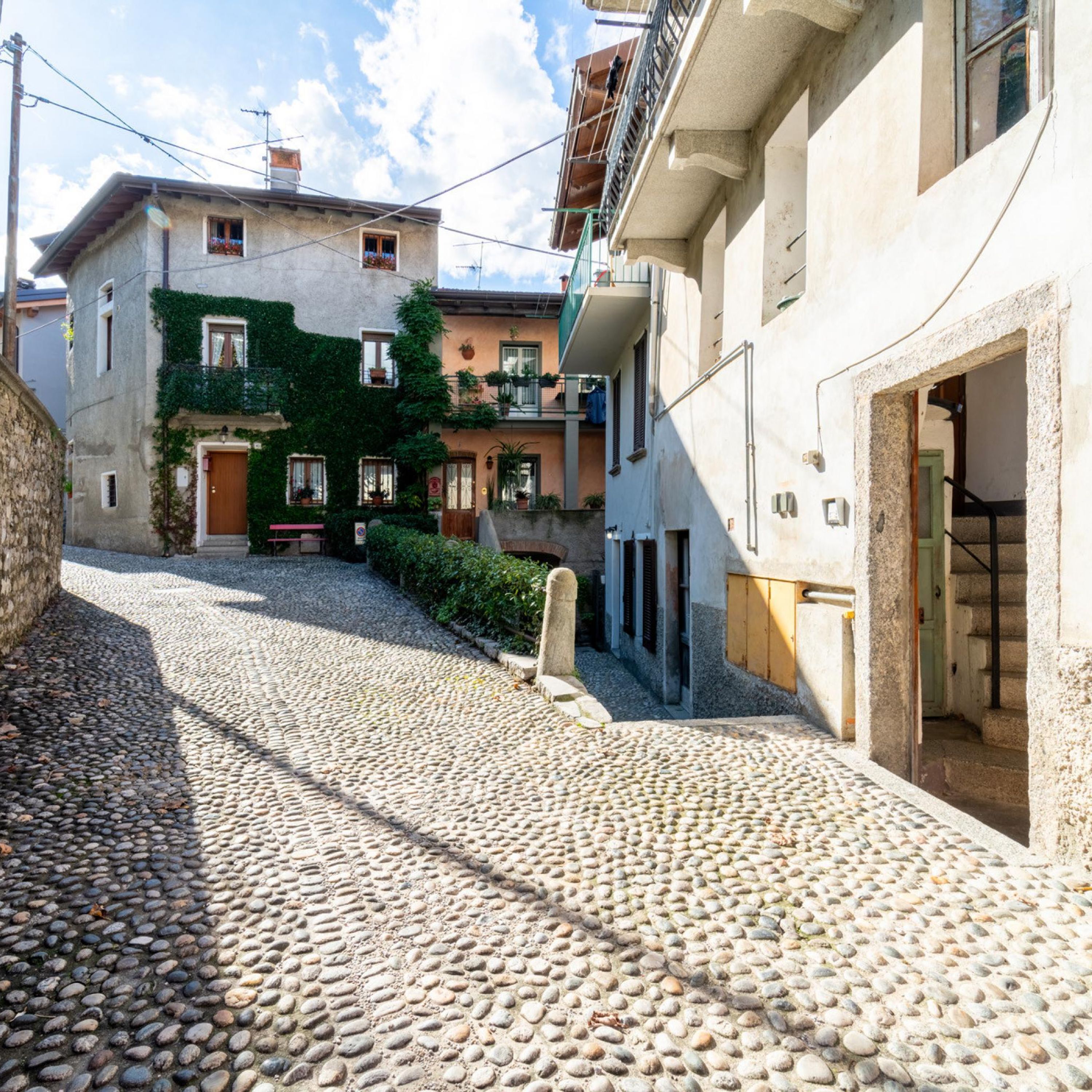 A cobblestone street with buildings on either side, featuring balconies and a mix of architectural styles.