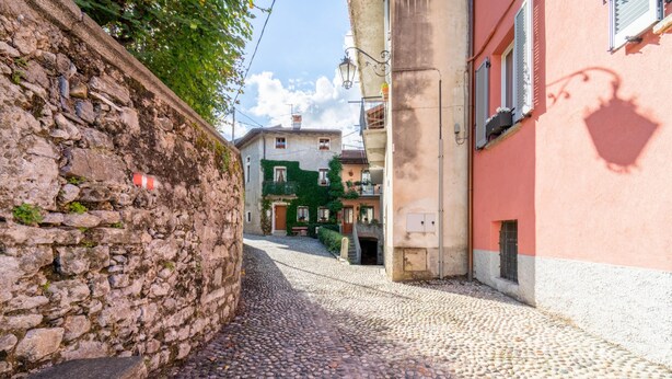 Een straat met kinderkopjes, met stenen muren en gebouwen met balkons en luiken.