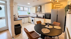 A modern kitchen with a dining area, including a table with woven placemats, a refrigerator, and a washing machine.