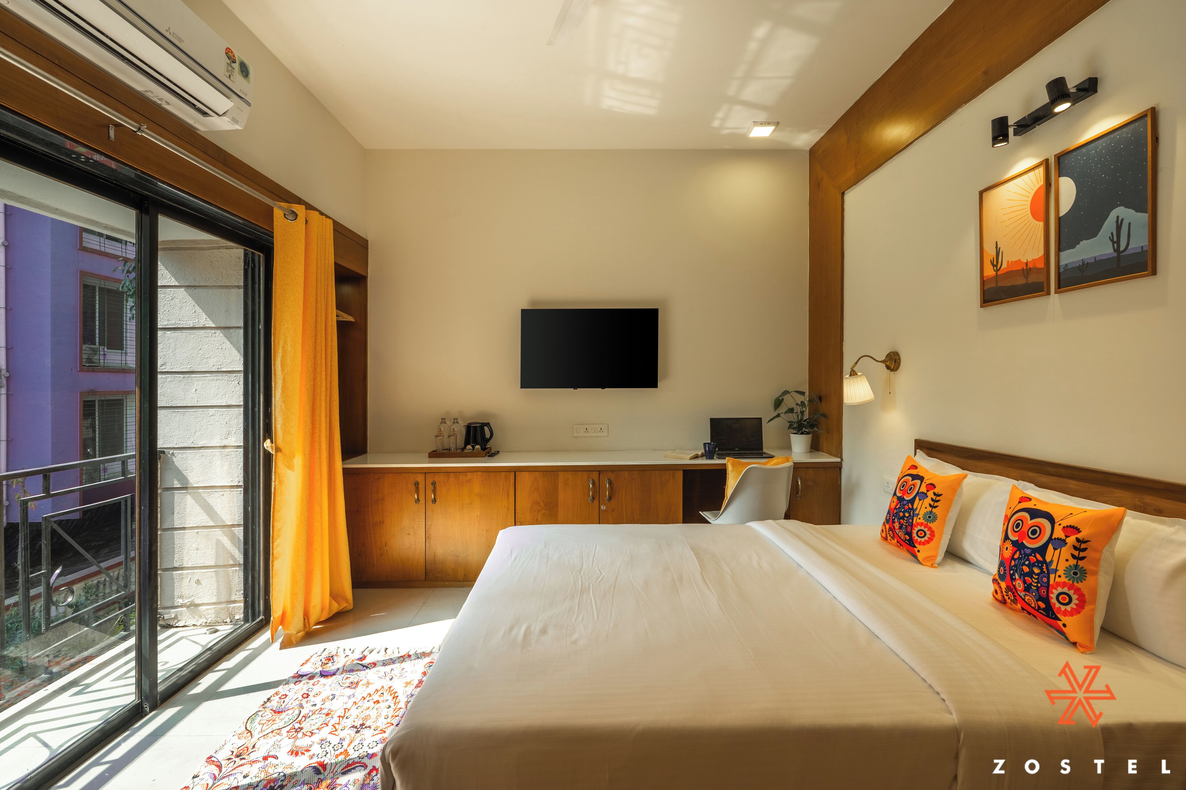 A hotel room with a bed, a TV, a desk, and a window with curtains.