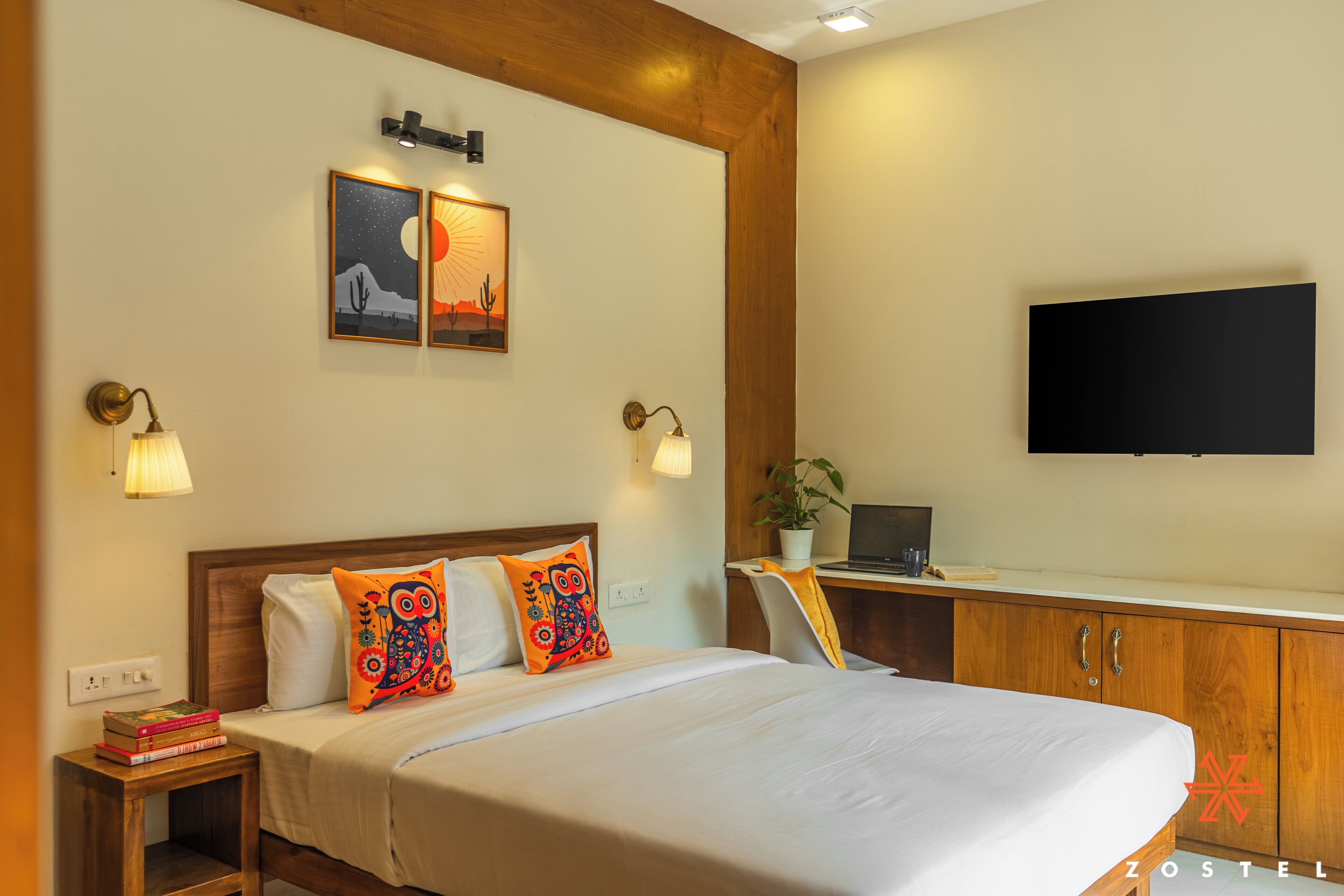 A hotel room with a bed, bedside tables, a desk, a TV, and artwork on the wall.