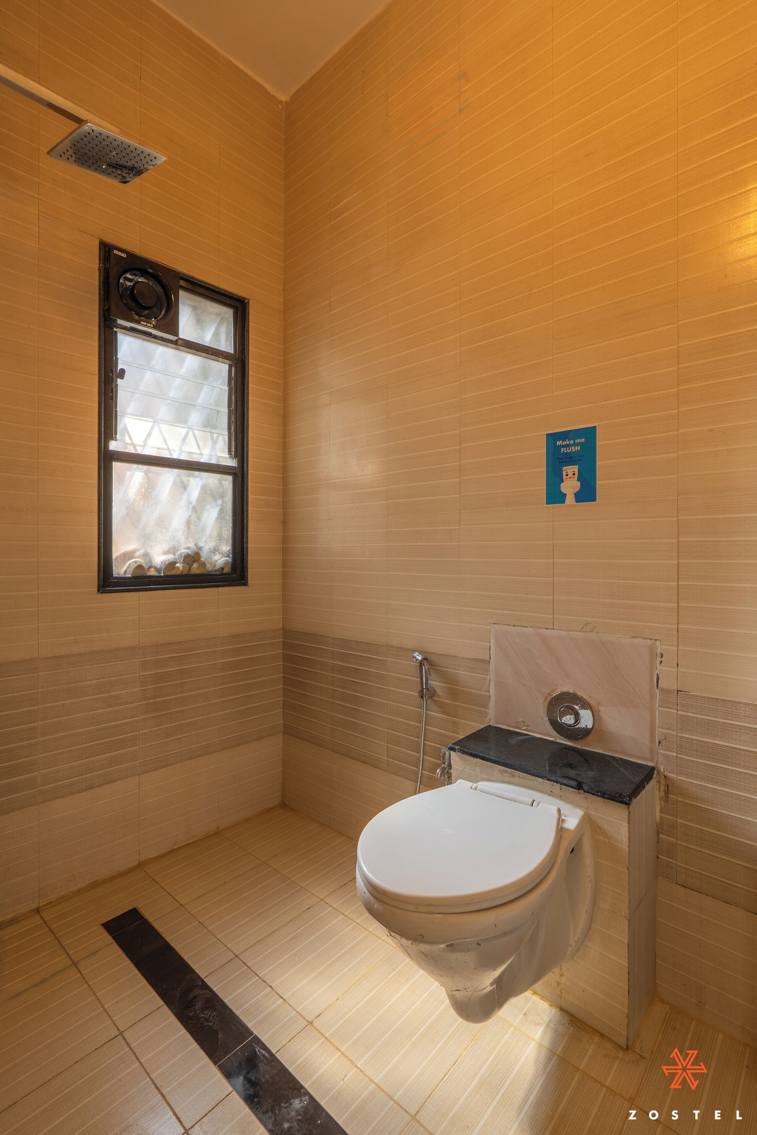 A small, tiled bathroom with a window, a toilet, and a showerhead.
