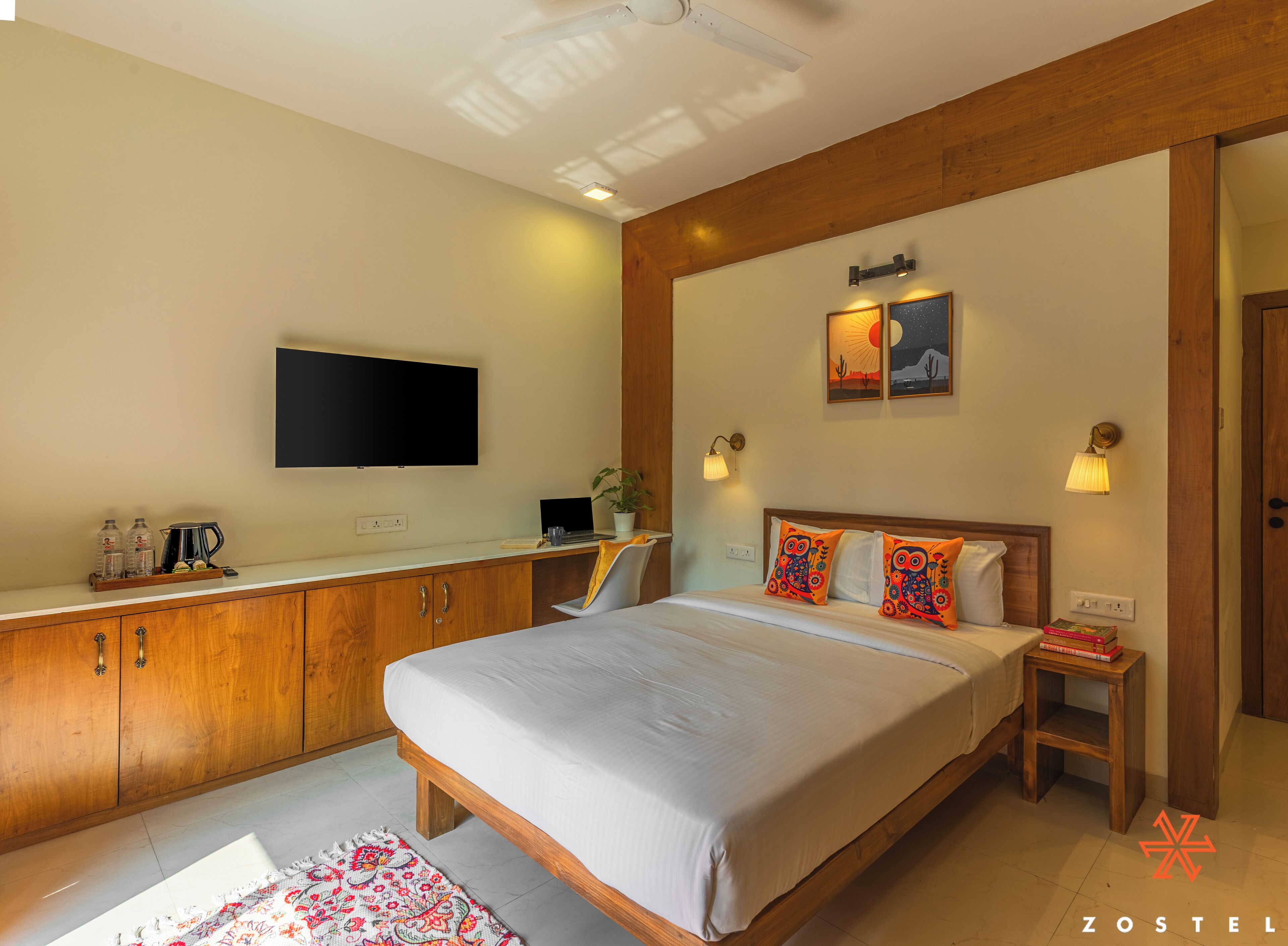 A hotel room with a bed, bedside table, lamp, and a flat-screen TV mounted on the wall.