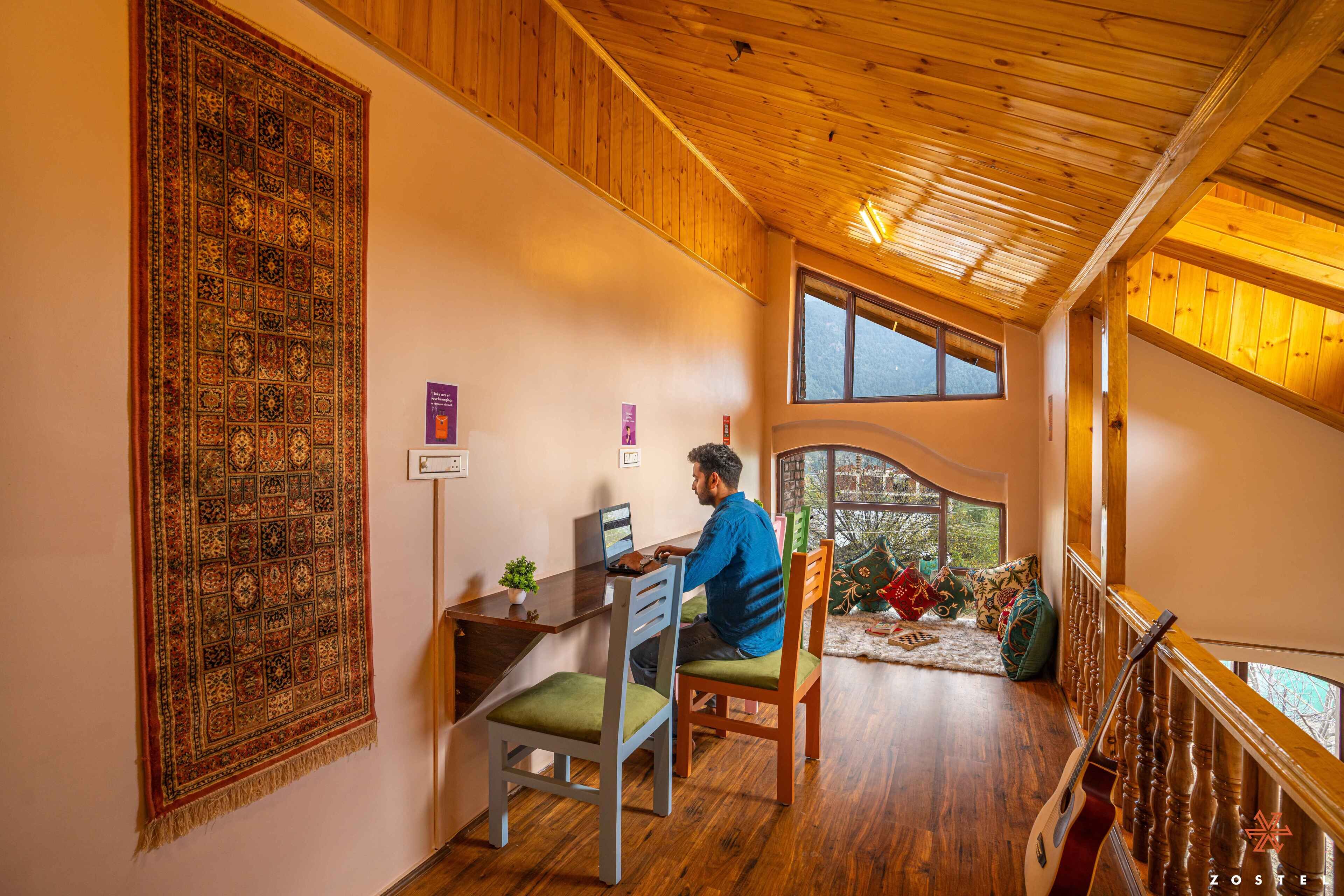 Une pièce avec un plafond en bois, un grand tapis, un bureau avec un ordinateur portable et une vue par la fenêtre.