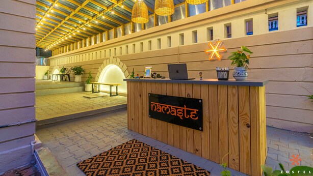 A reception desk with a sign reading "Namaste" and a modern interior with wicker pendant lights and a patterned rug. - Zostel Pune (Pune)