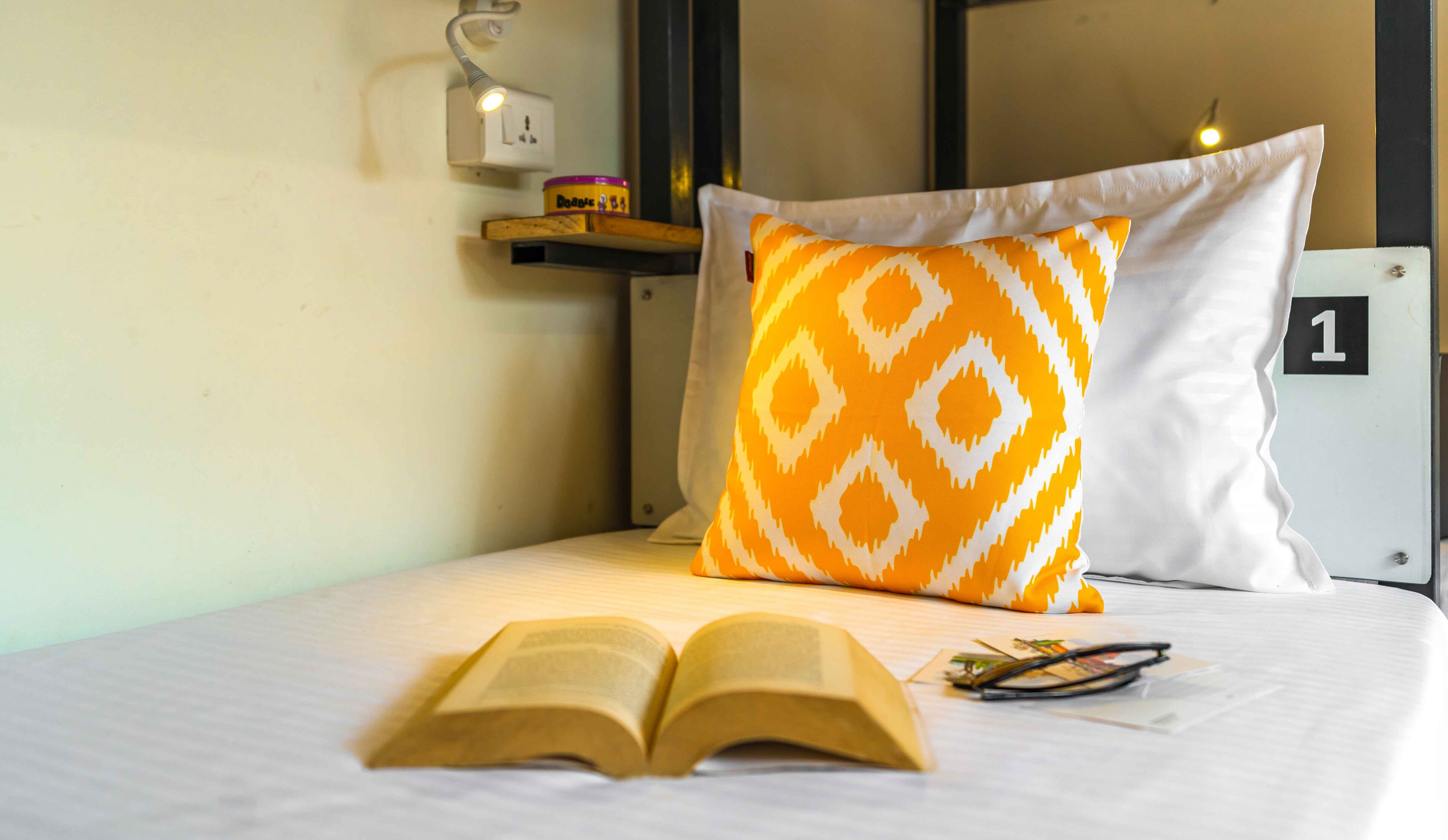 Un lit bien fait, avec un oreiller à motifs, un livre ouvert et une paire de lunettes posées sur le lit.