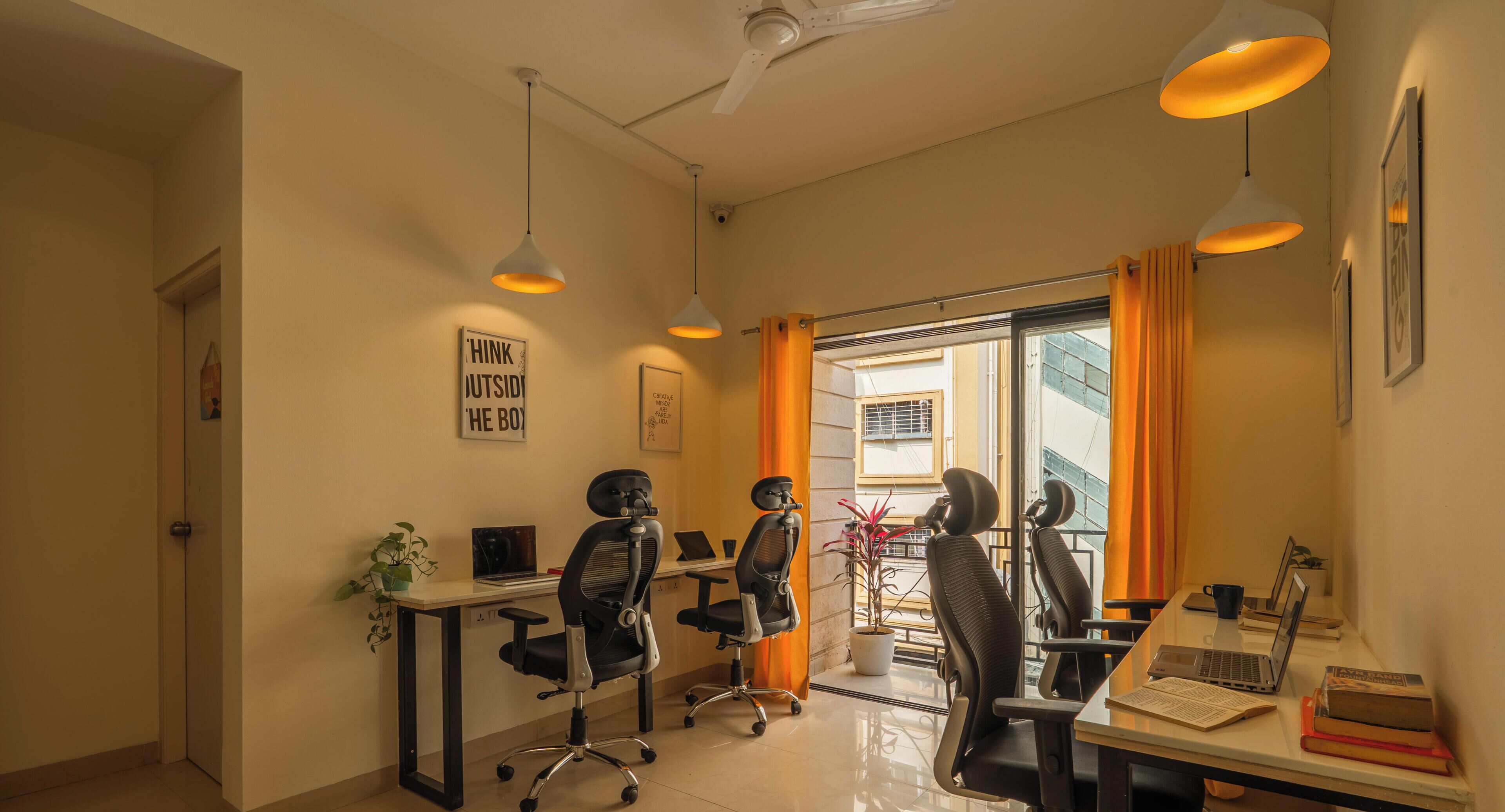 A modern office space with two desks, office chairs, and pendant lighting.