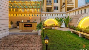 A hotel lobby with a reception desk, a covered outdoor seating area, and a well-maintained garden with a statue. - Zostel Pune (Pune)
