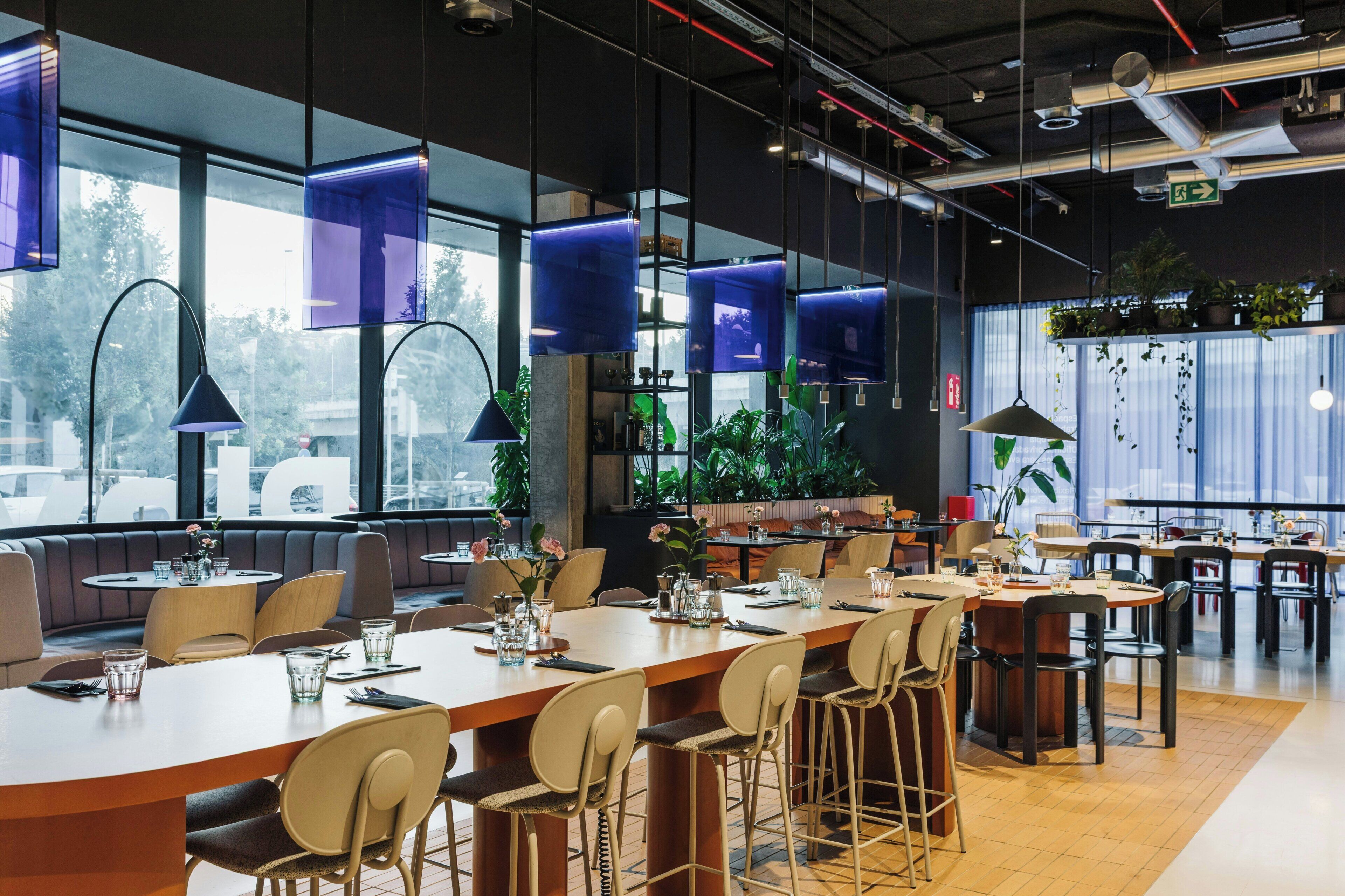 Un restaurant moderne doté de grandes fenêtres, de suspensions lumineuses bleues et offrant différents types d’aménagements pour s’asseoir.