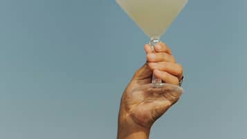 Una mano sosteniendo una copa de martini contra un cielo despejado.