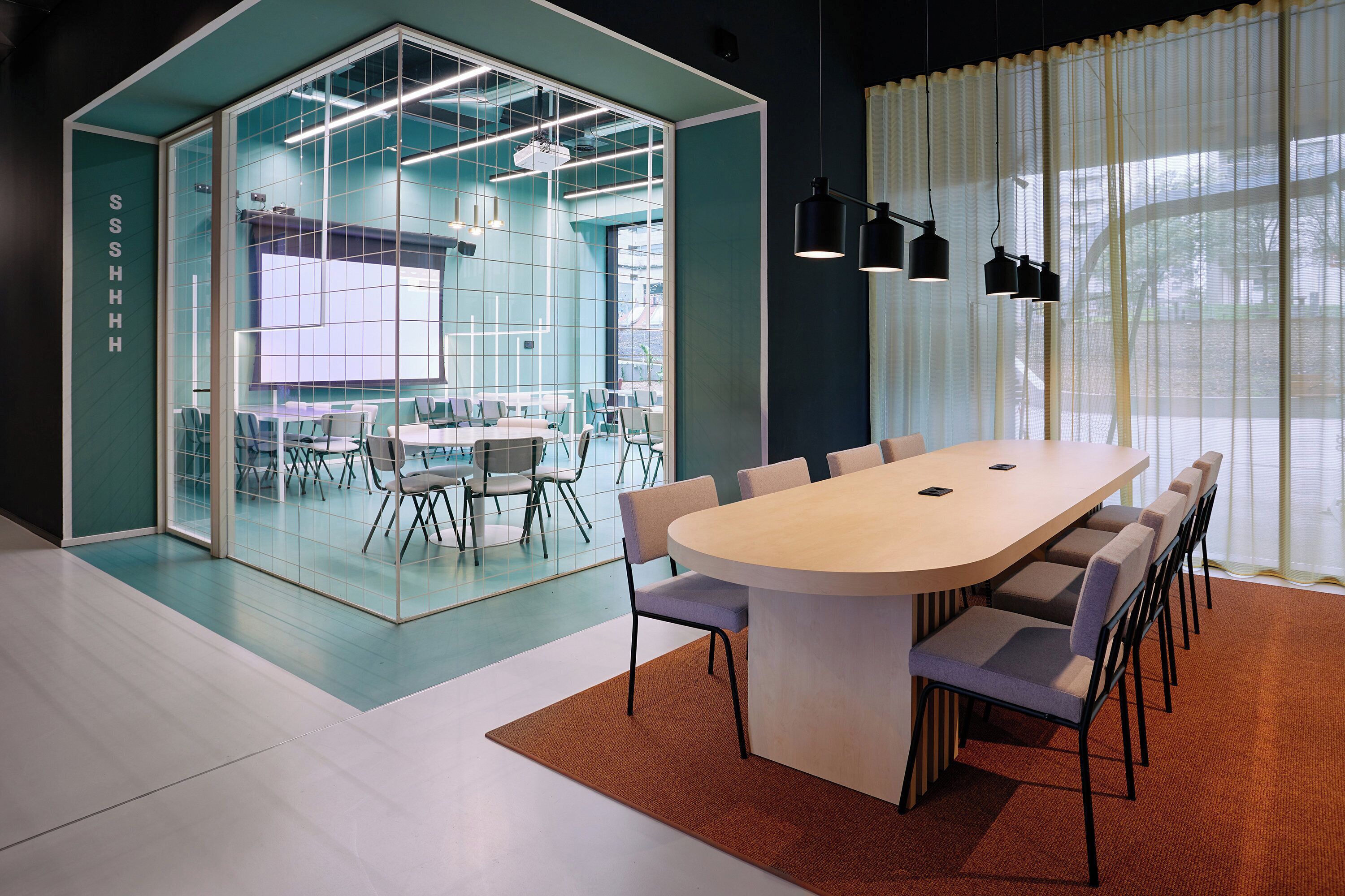 A modern conference room with a large table, chairs, and a glass partition separating it from another room.