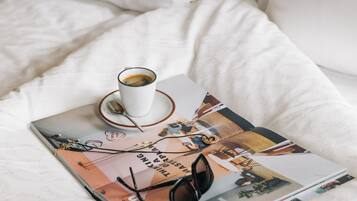 Una cama bien hecha con ropa blanca, una taza de café y una revista encima.