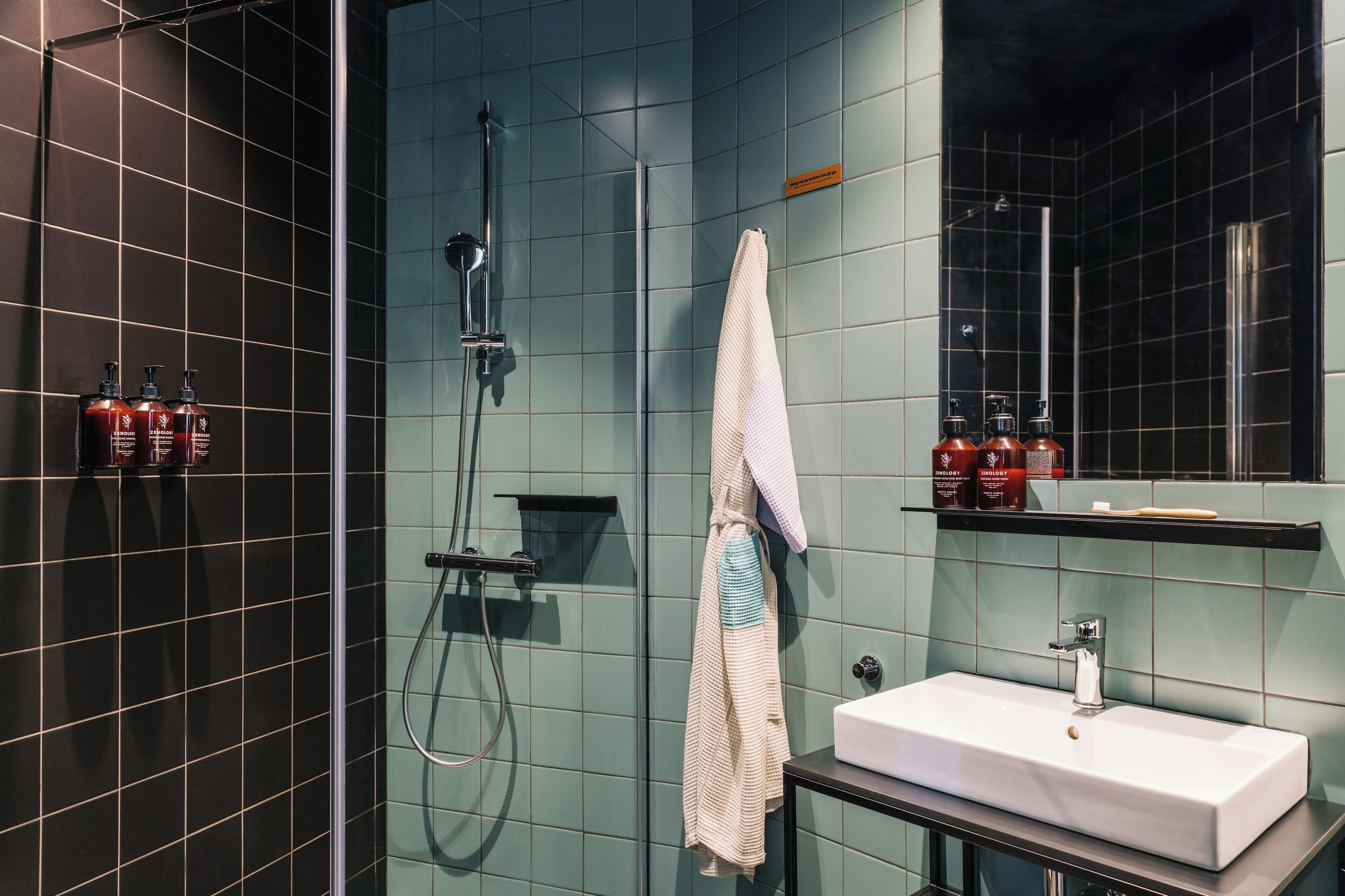 Un baño moderno con ducha de vidrio, lavamanos blanco y artículos de aseo en un estante.