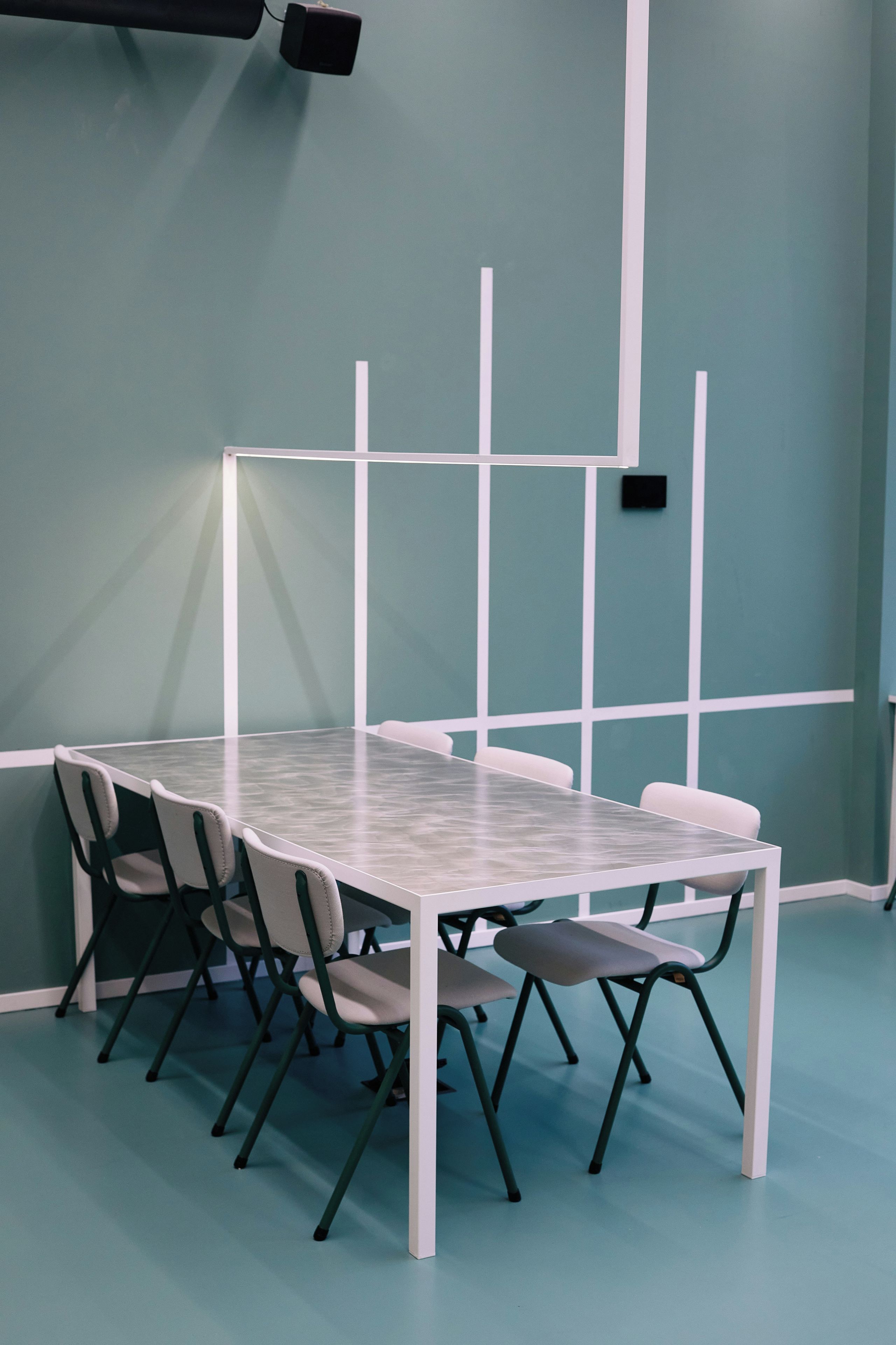 Un salón de conferencias con una mesa de vidrio, sillas blancas y una pared azul claro.