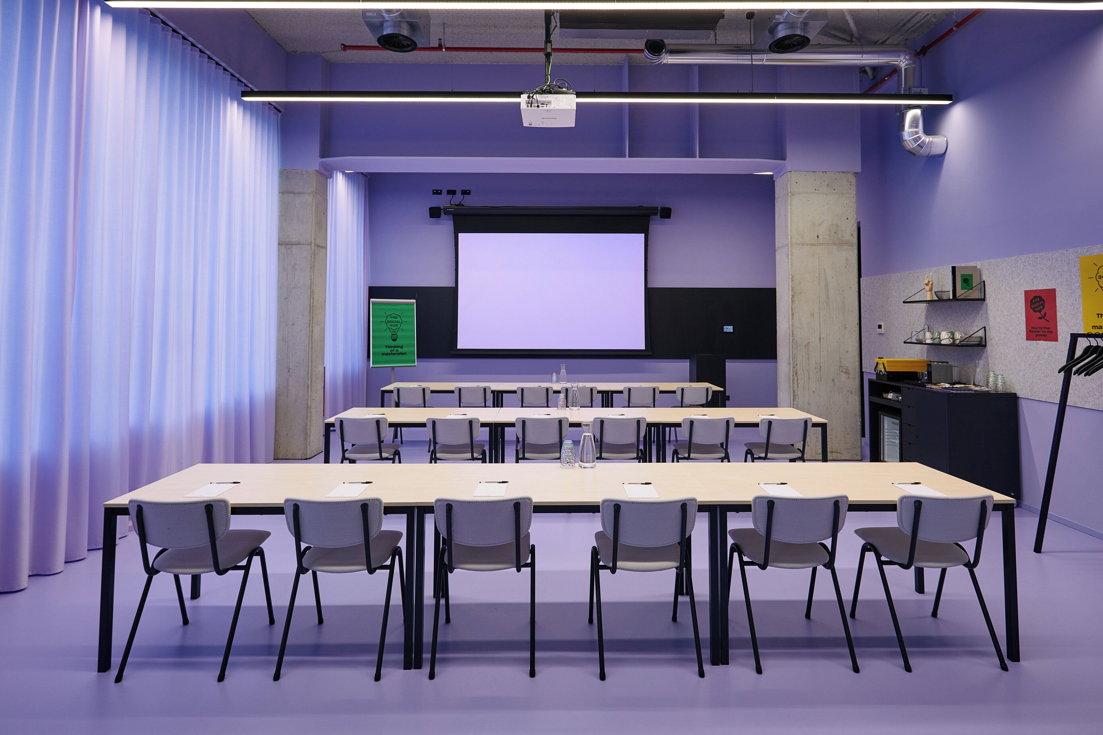 Ein Konferenzraum mit einem großen Tisch, Stühlen, einer Projektionsfläche und einem Präsentationsbildschirm.