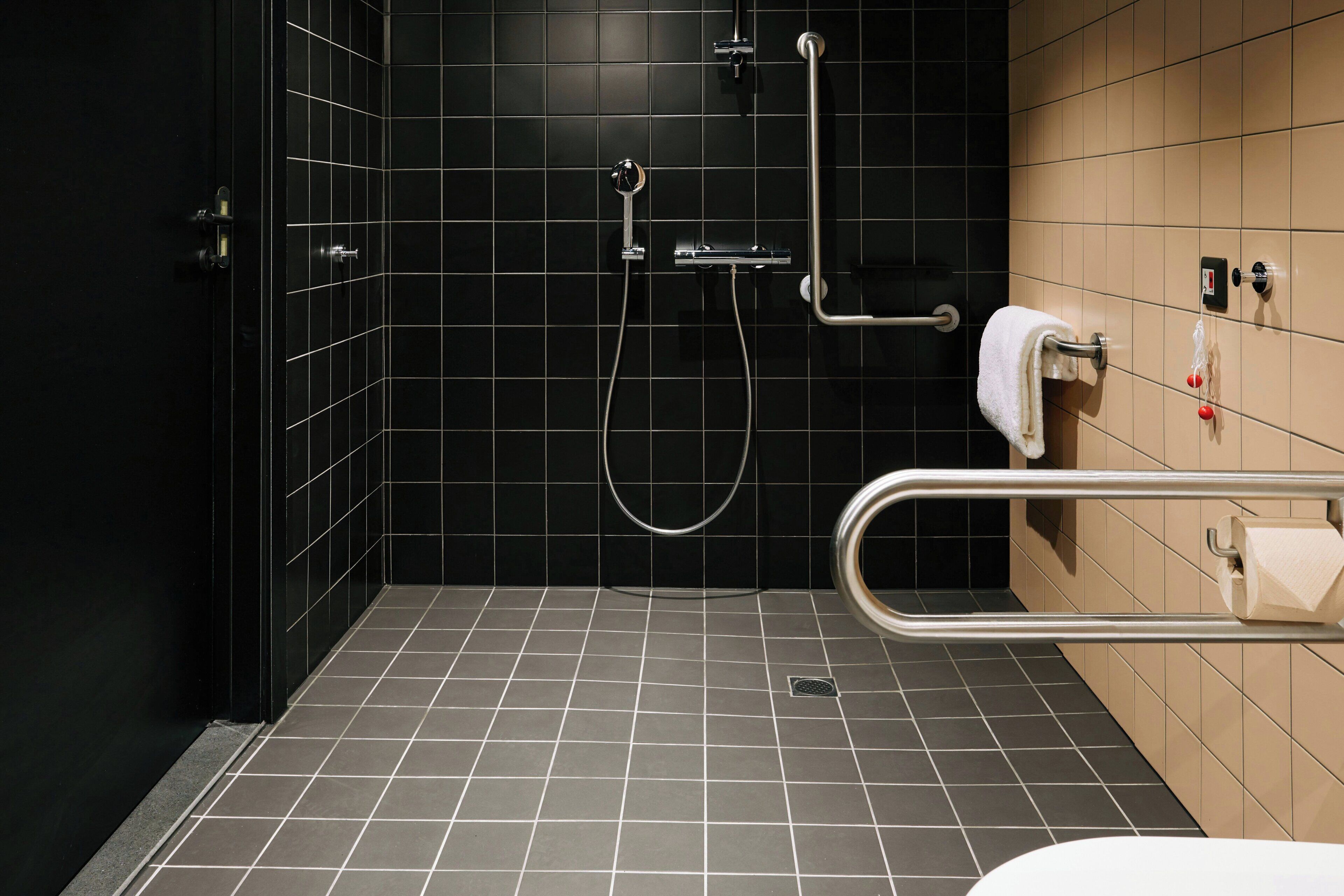A bathroom with black tiled walls, a shower with a handheld showerhead, a grab bar, and a towel rack.