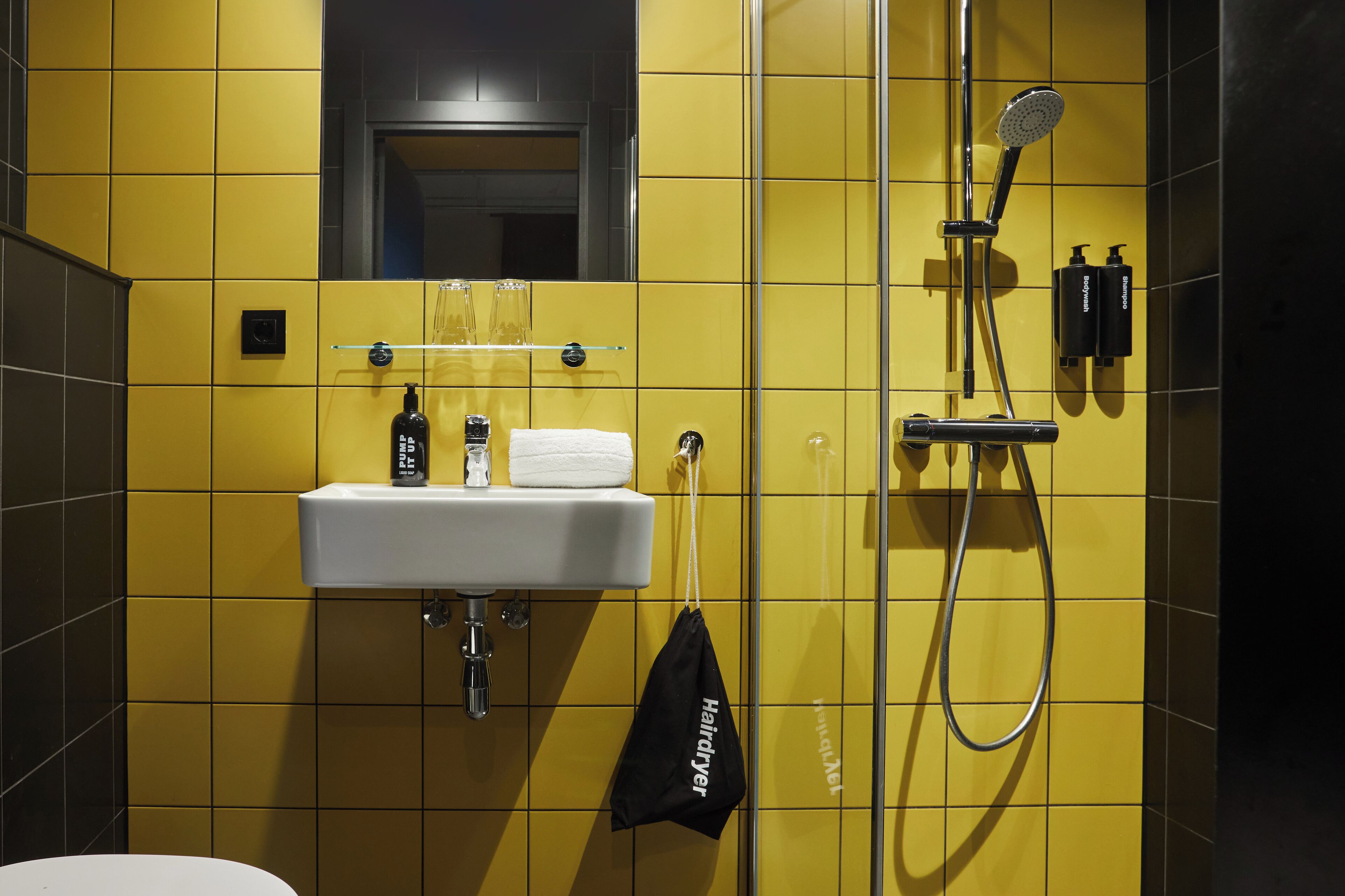 A bathroom with yellow tiles, a white sink, a handheld showerhead, and a towel hanging on a rack.